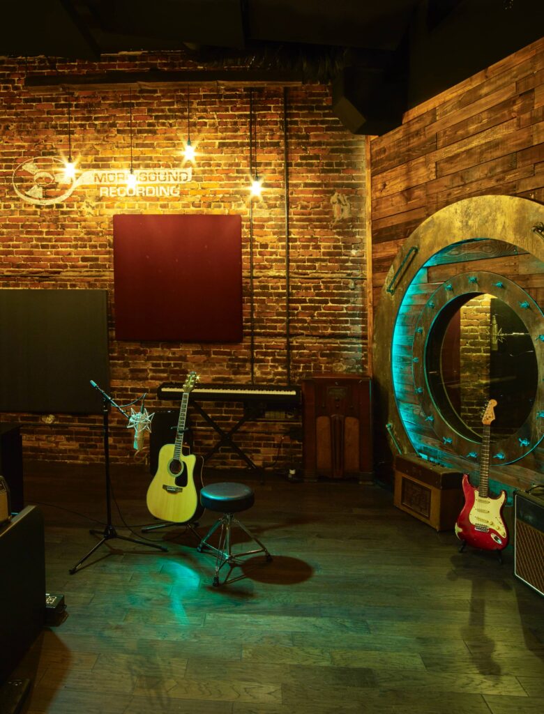 Tracking space at Morrisound Recording. It shows the original brick wall with original Morrisound logo, 2 guitars, and the port-hole styled glass into the large isolation booth.